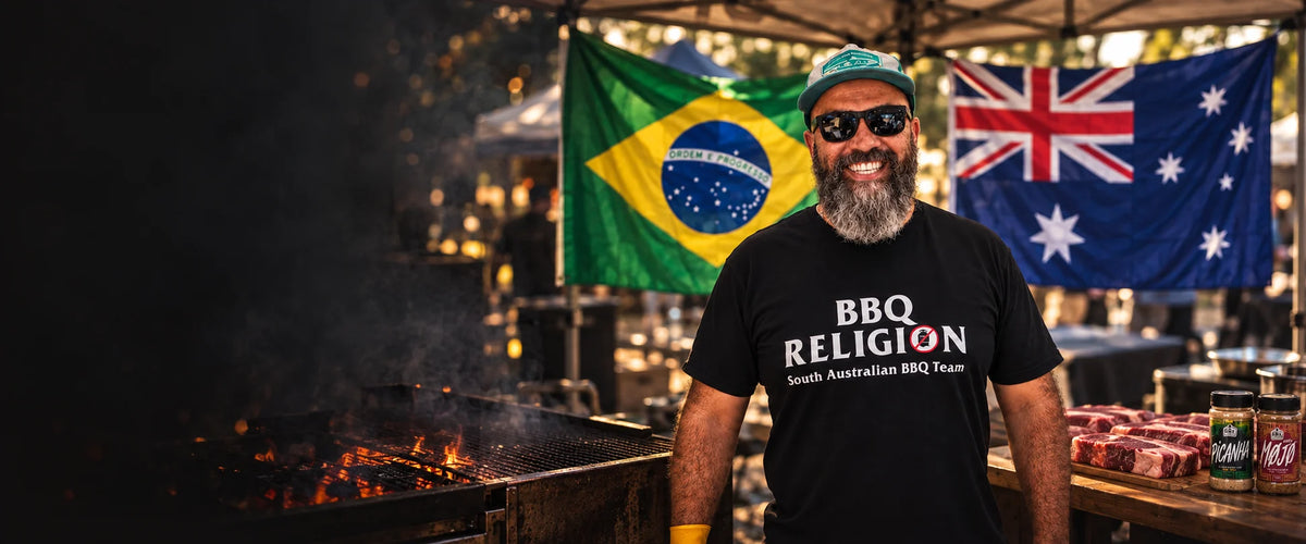 Adriano wearing his BBQ Religion tee with Brazilian and Australian flags, a charcoal barbecue and a prep table with steaks and rubs