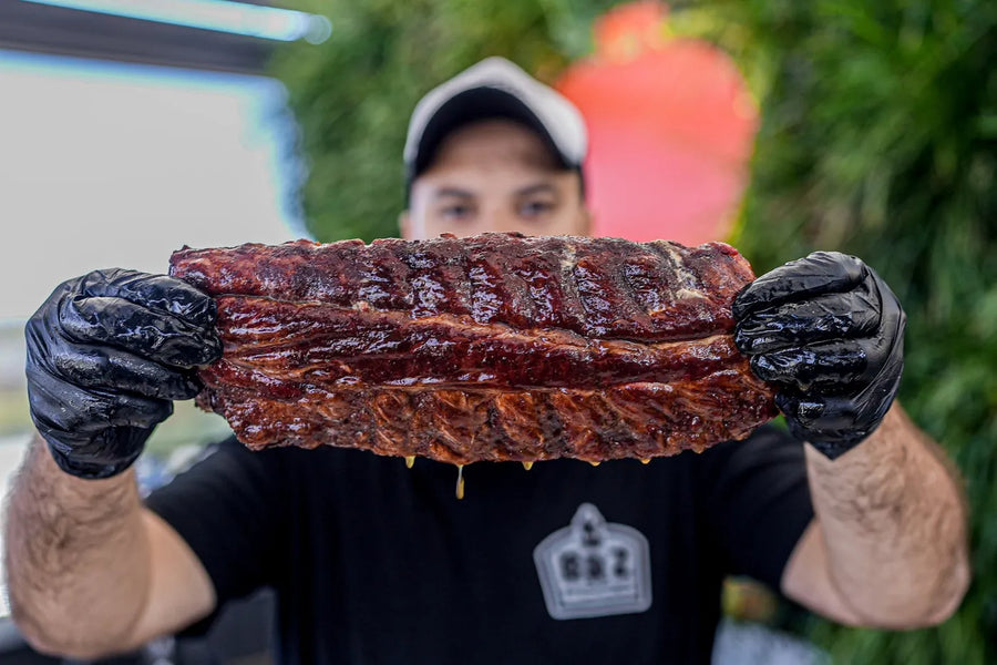 A rack of pork ribs, glazed and dripping, held up in two gloved hands