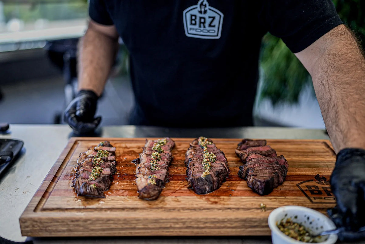 Four sliced steaks topped with chimichurri on a BRZ Food board